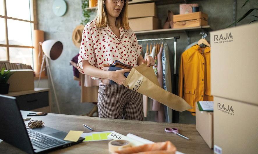 Vrouw steekt een kledingstuk in een papieren verzendzak van RAJA