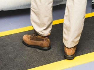 Man met bruine werkschoenen staat op antivermoeidheidsmat